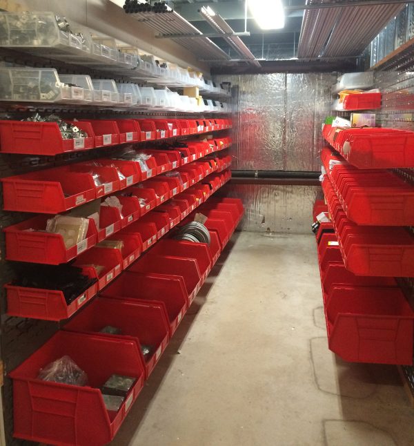 Louvered panels with red plastic bins attached storing materials in a warehouse setting.