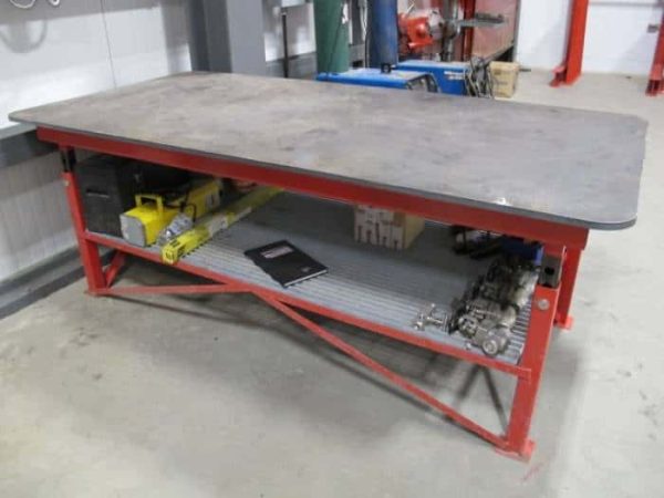 Red heavy duty welding table with a steel top in a warehouse setting.