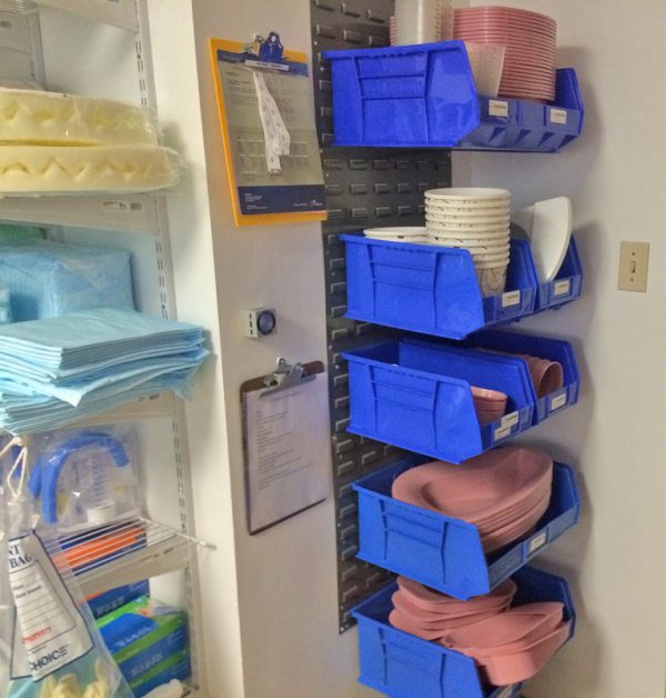 Plastic stackable bins attached to louvered panels storing medical supplies in a hospital setting.