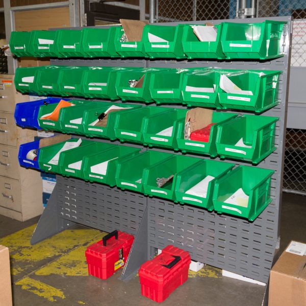 Louvered panel with plastic bins attached storing mail in a warehouse setting.